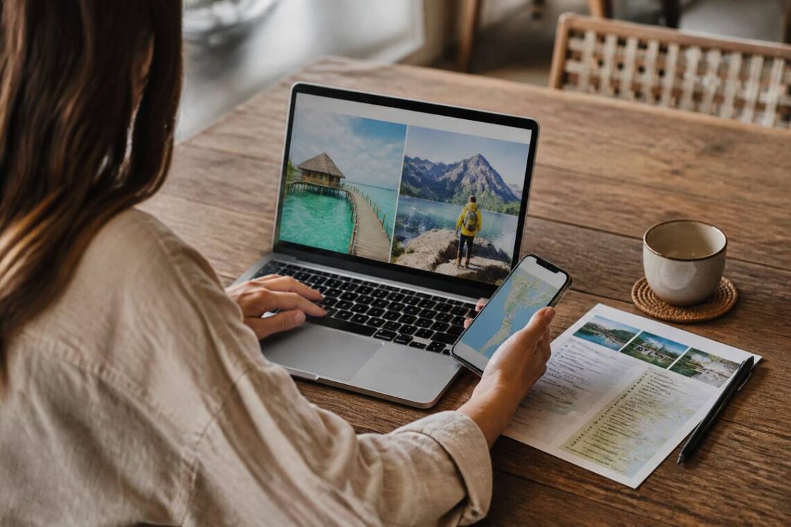 Iemand vergelijkt reisopties op laptop en telefoon aan tafel, bij daglicht.